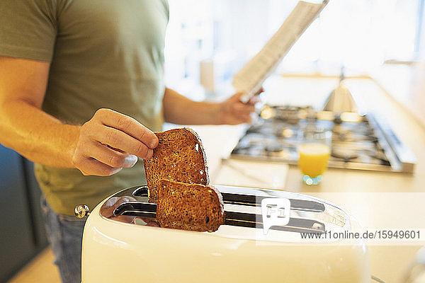 Close up man making toast and reading newspaper in morning kitchen