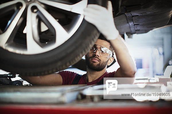 Männlicher Mechaniker unter dem Auto  untersucht Reifen in Autowerkstatt