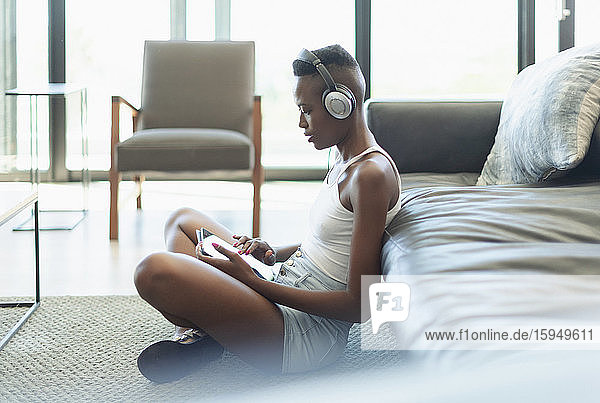 Junge Frau  die im Wohnzimmer mit Kopfhörern und digitalem Tablet Musik hört