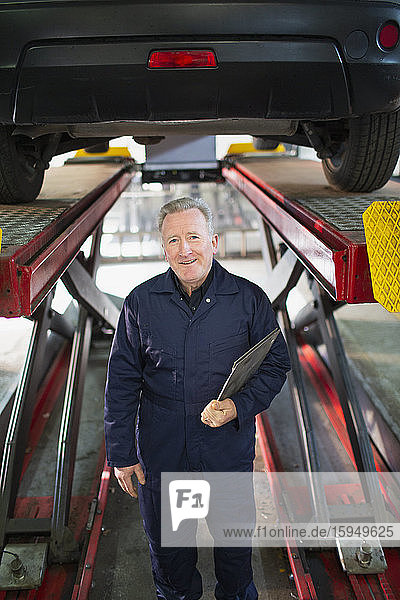 Portrait confident male mechanic under car in auto repair shop