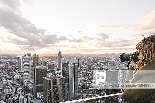 Germany  Hesse  Frankfurt  Woman photographing city downtown at sunset