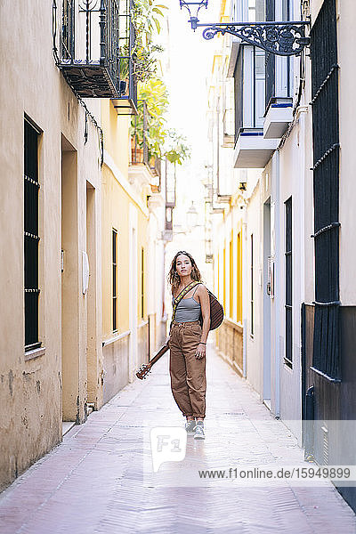 Porträt einer jungen Frau mit Gitarre in einer engen Straße inmitten von Gebäuden in Santa Cruz  Sevilla  Spanien