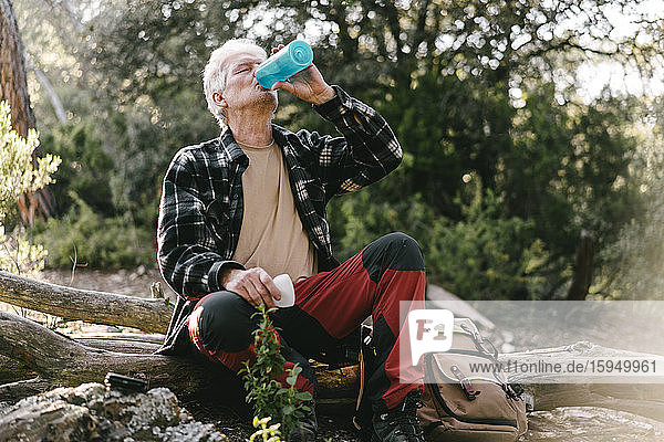 Wanderer mit Rucksack macht Pause und trinkt Wasser aus der Flasche