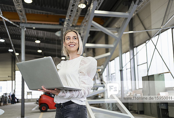 Smiling young woman using laptop in a factory