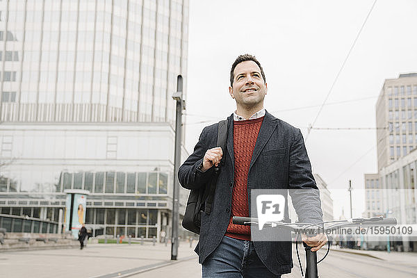 Lächelnder Geschäftsmann schaut weg  während er mit dem Fahrrad auf der Stadtstraße in Frankfurt am Main unterwegs ist