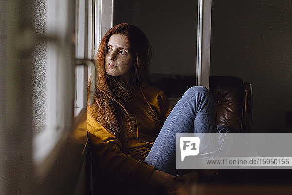 Portrait of redheaded woman sitting at open window looking at home looking at distance
