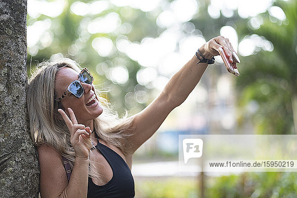Schöne Frau lehnt mit Smartphone an Baumstamm  Costa Rica