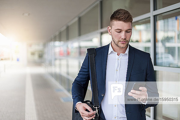 Porträt eines jungen Geschäftsmannes in der Stadt  der sein Smartphone überprüft