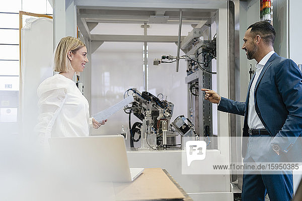 Geschäftsmann und junge Frau im Gespräch an einer Maschine in einer Fabrik
