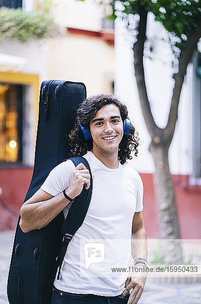 Portrait of confident young man carrying guitar in bag while standing on street  Santa Cruz  Seville  Spain