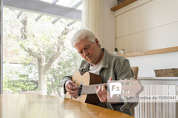 Älterer Mann zupft Gitarrensaiten beim Üben zu Hause