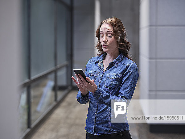 Überraschte Geschäftsfrau benutzt Handy in moderner Büroetage