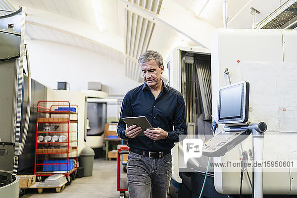 Reifer Mann arbeitet in der Produktionshalle einer Fabrik mit einem digitalen Tablett
