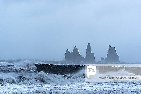 Island  Hofn  Meereswellen prasseln gegen eine Steinmauer an der Küste  im Hintergrund Stapelfelsen