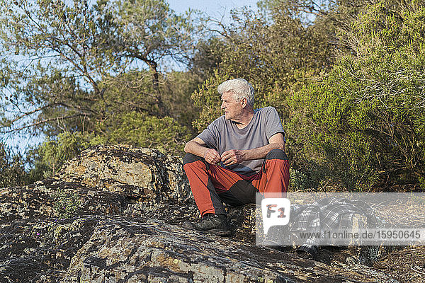 Älterer Mann sitzt auf einem Felsen in der Natur