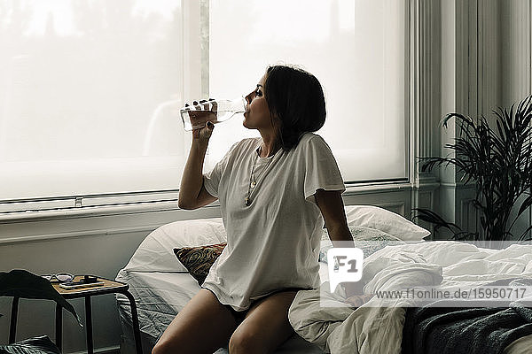 Reife Frau sitzt morgens im Bett und trinkt Wasser