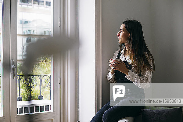 Nachdenkliche Geschäftsfrau schaut durchs Fenster  während sie im Büro Kaffee trinkt