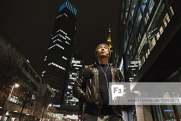Portrait of stylish man with yellow hat and earphones in the city at night