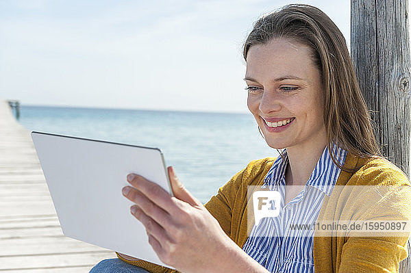 Porträt einer glücklichen Frau  die mit einem digitalen Tablet auf einem Steg sitzt  Mallorca  Spanien