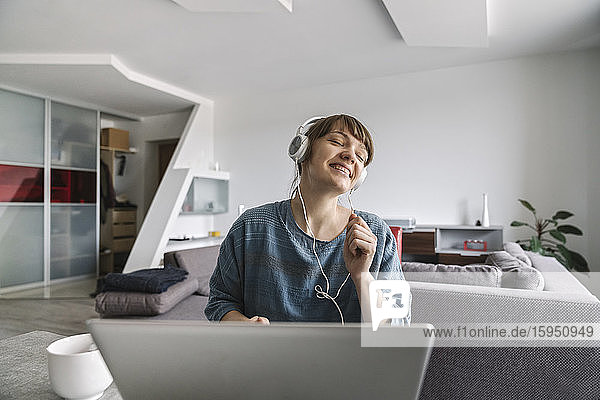 Happy woman wearing headphones and using laptop at home