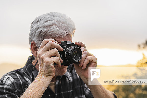 Älterer Mann auf einer Wanderung bei Sonnenuntergang beim Fotografieren