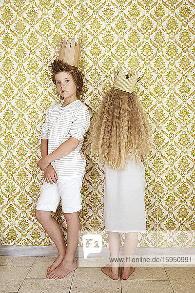 Boy and girl standing at a wall wearing cardboard crowns