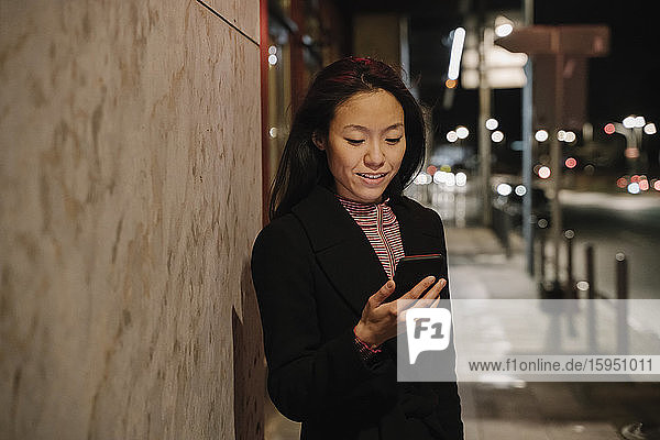 Young woman using smartphone in the city at night  Frankfurt  Germany