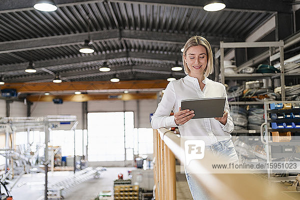 Lächelnde junge Frau mit Tablette in einer Fabrik
