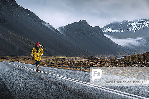 Iceland  Woman in yellow coat running along remote Icelandic highway