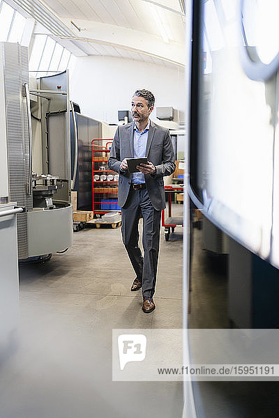 Mature businessman walking on production floor of factory  using digital tablet