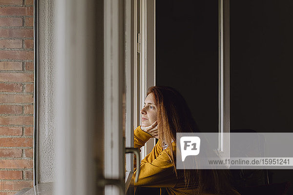 Redheaded woman at open window looking at distance