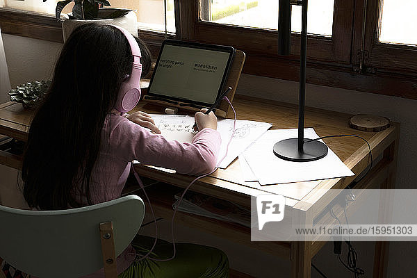 Girl with headphones drawing manga comics while using tablet computer at desk in house