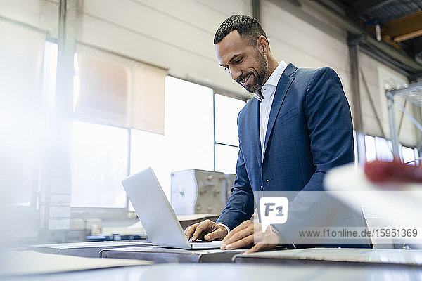 Smiling businessman using laptop in a factory