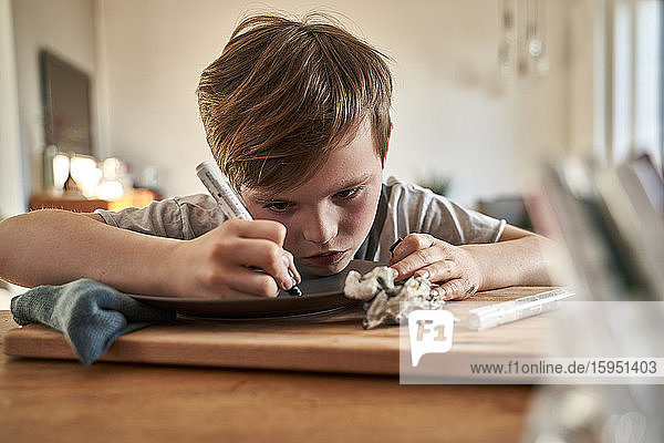 Fokussierter Junge malt zu Hause Teller mit Porzellanfarbe