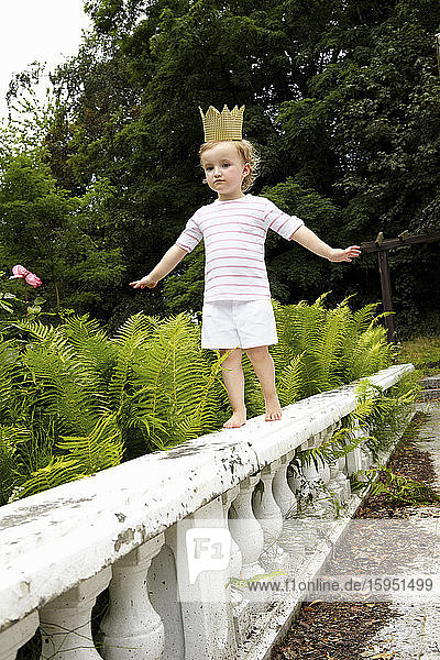 Kleines Mädchen  das auf einer Balustrade läuft und eine Pappkrone trägt