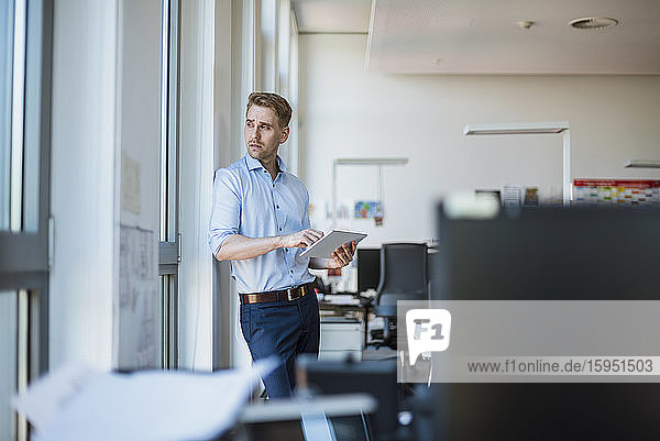 Businessman standing at the window in office using tablet
