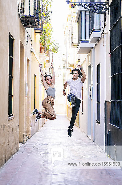 Sorgenfreies Paar in voller Länge springt während des Urlaubs in Santa Cruz  Sevilla  Spanien  auf der schmalen Straße