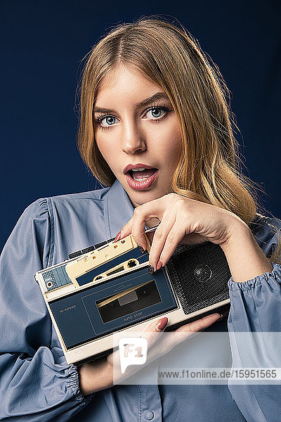 Blond woman with cassette player in front of blue background
