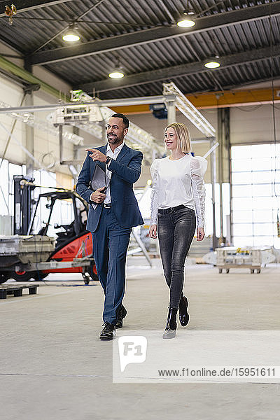 Businessman and young woman walking and talking in a factory