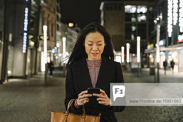 Junge Frau  die nachts in der Stadt ein Smartphone benutzt  Frankfurt  Deutschland