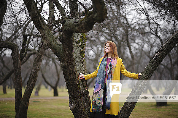 Lächelnde  nachdenkliche Frau balanciert auf kahlem Baum im Park