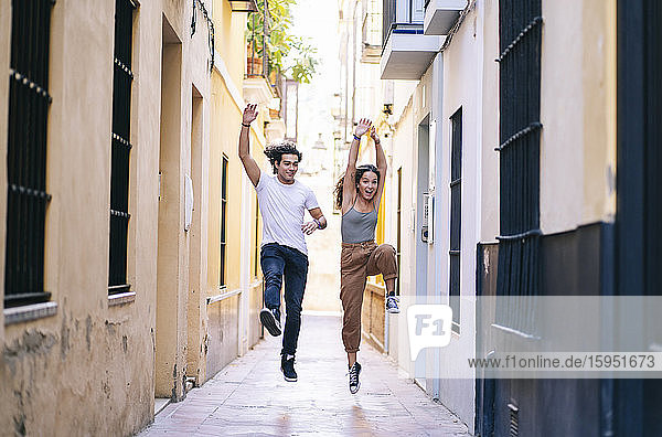 Unbeschwertes junges Paar springt in voller Länge auf der schmalen Straße von Santa Cruz  Sevilla  Spanien