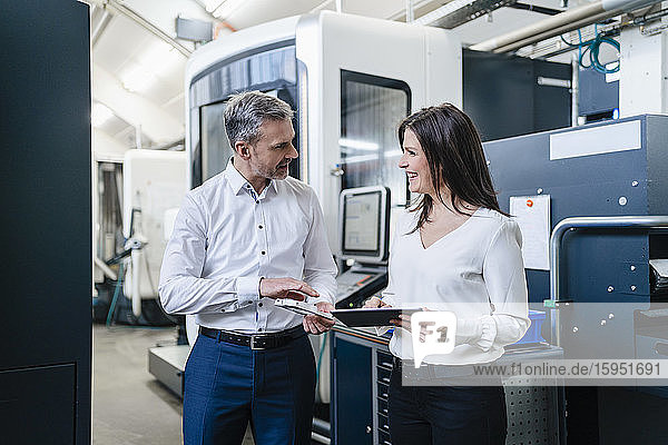 Geschäftsmann und Geschäftsfrau mit Produkt und Tablette bei einem Arbeitstreffen in einer Fabrik