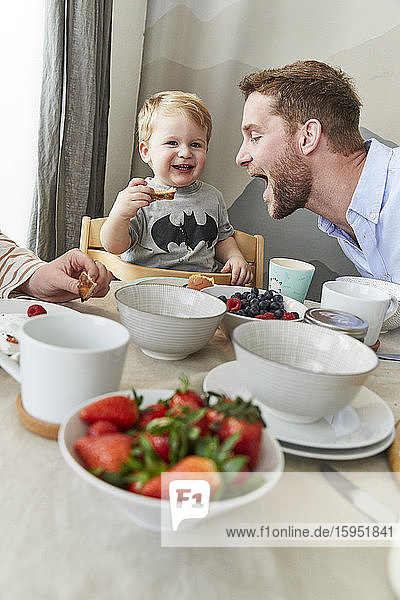 Portrait of happy little boy having fun at breakfast table with his father