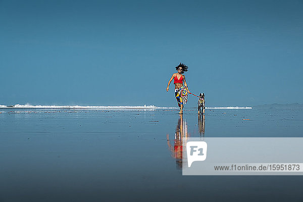 Unbeschwerte junge Frau geht mit ihrem Hund am Strand spazieren  Costa Rica