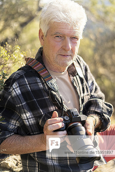 Porträt eines älteren Mannes mit Kamera in der Natur
