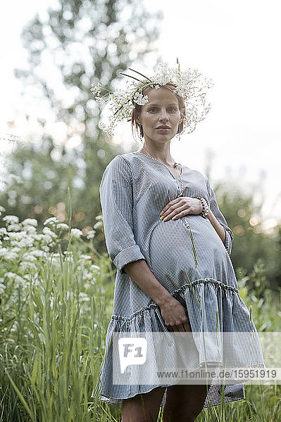 Porträt einer schwangeren Frau mit Händen auf dem Bauch im Park stehend