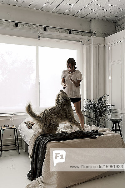 Reife Frau steht auf dem Bett und spielt mit ihrem Hund