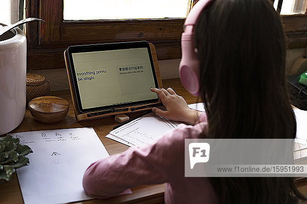 Mädchen mit Kopfhörern übersetzt Sprachen auf digitalem Tablet  während sie zu Hause Comics lernt