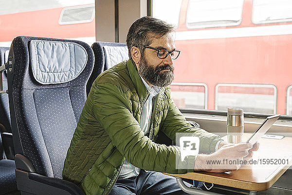 Mann sitzt mit Tablette im Zug